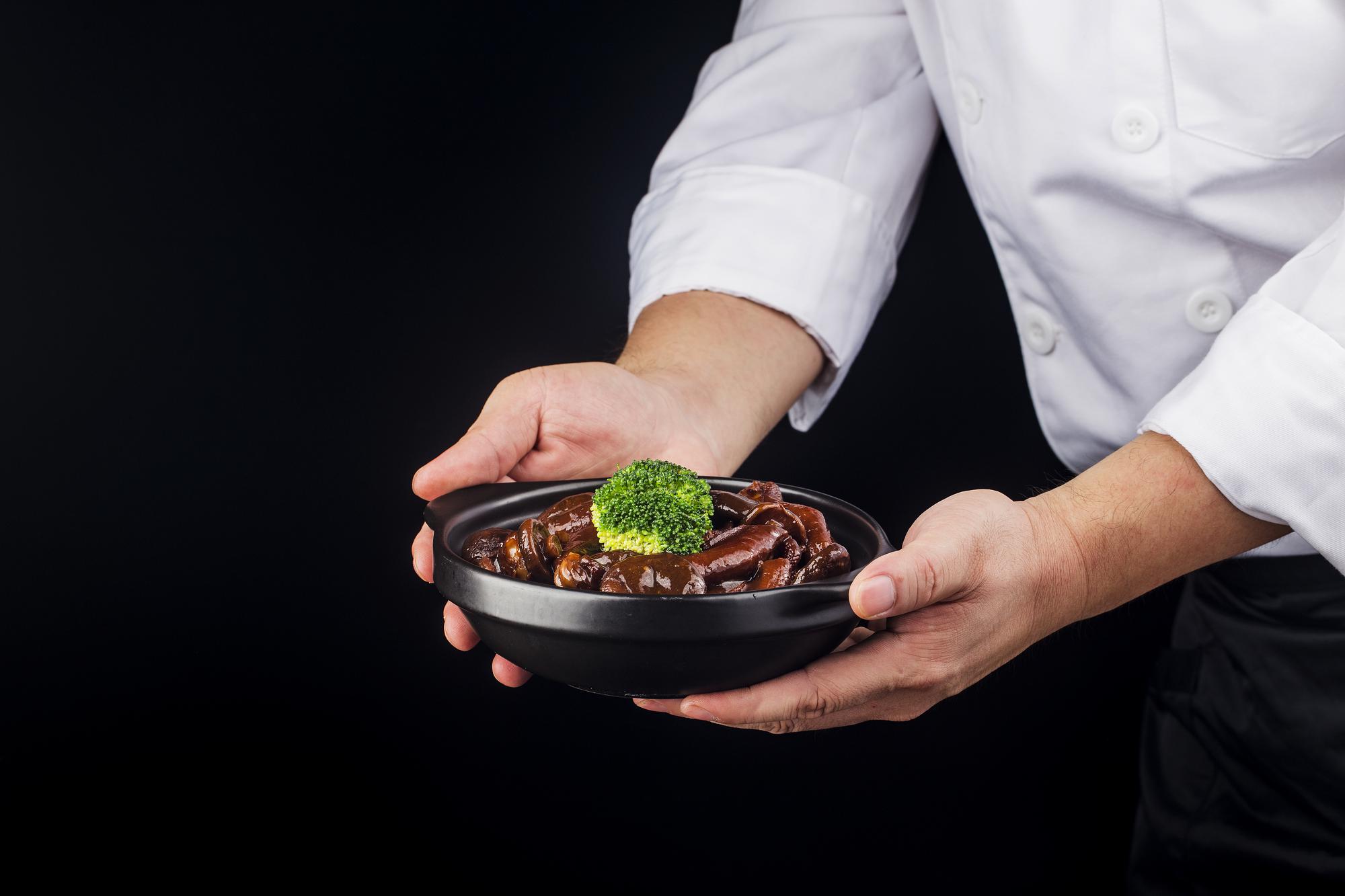 chef plating a composed dish on a dark counter